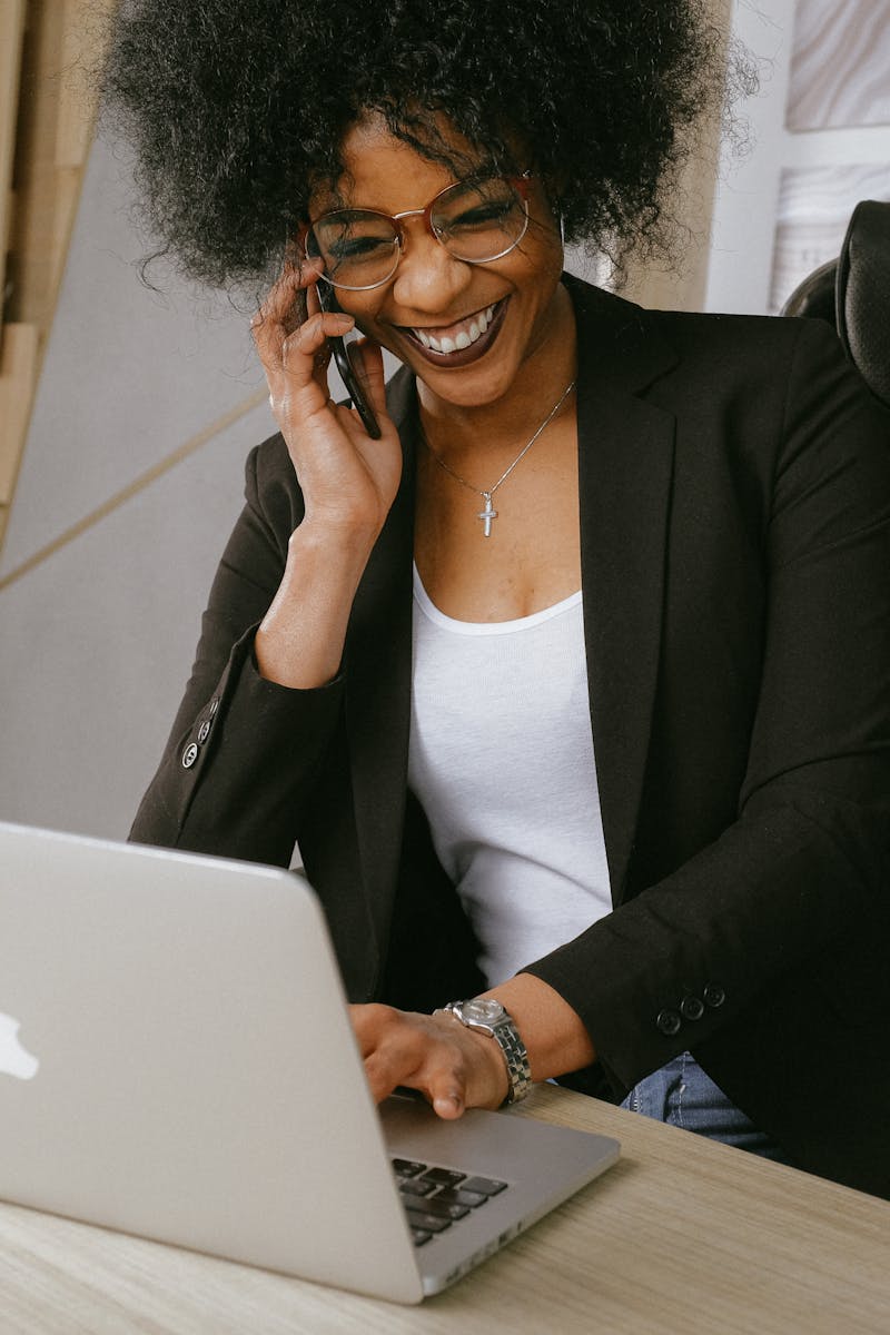 Smiling woman on phone call while working on a laptop in a stylish office.